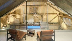 A loft-style room with a sloped ceiling, wooden beams, and a large window. There are two leather chairs and a small wooden table.