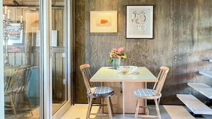 A dining area with a glass partition, a table with chairs, and two framed artworks on the wall.