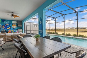 Ein Poolbereich mit Holztisch, Korbstühlen, Deckenventilator und Blick auf Pool und Landschaft.