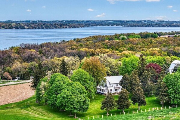 A large house surrounded by a well-maintained lawn and trees, with a lake in the background.