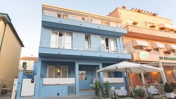 Un edificio de dos pisos con fachada azul, un balcón y zona de estar exterior con sombrillas.