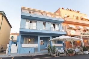A two-story building with a blue facade, a balcony, and outdoor seating with umbrellas.