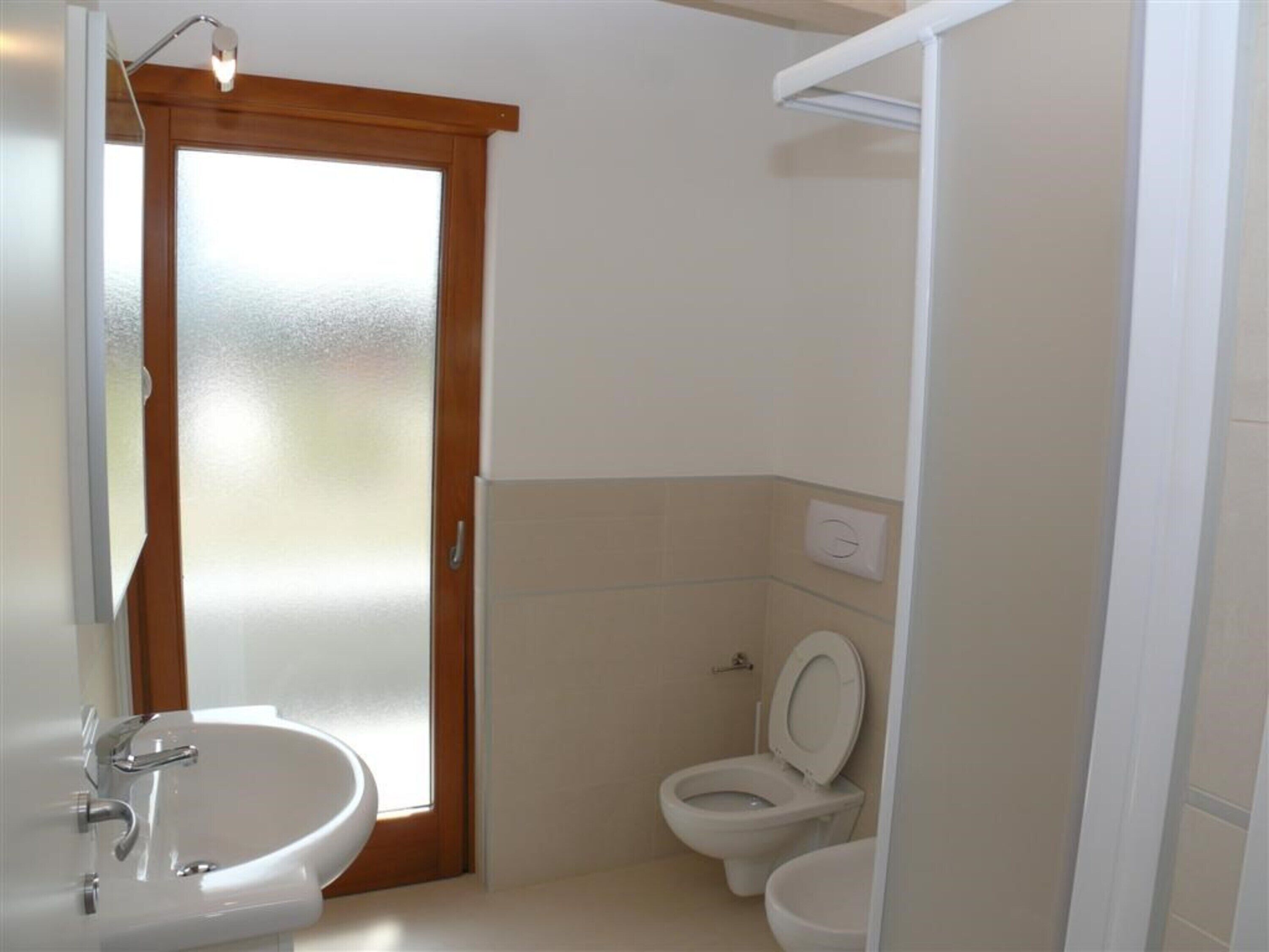 Un bagno con lavandino bianco, WC e porta in vetro satinato.