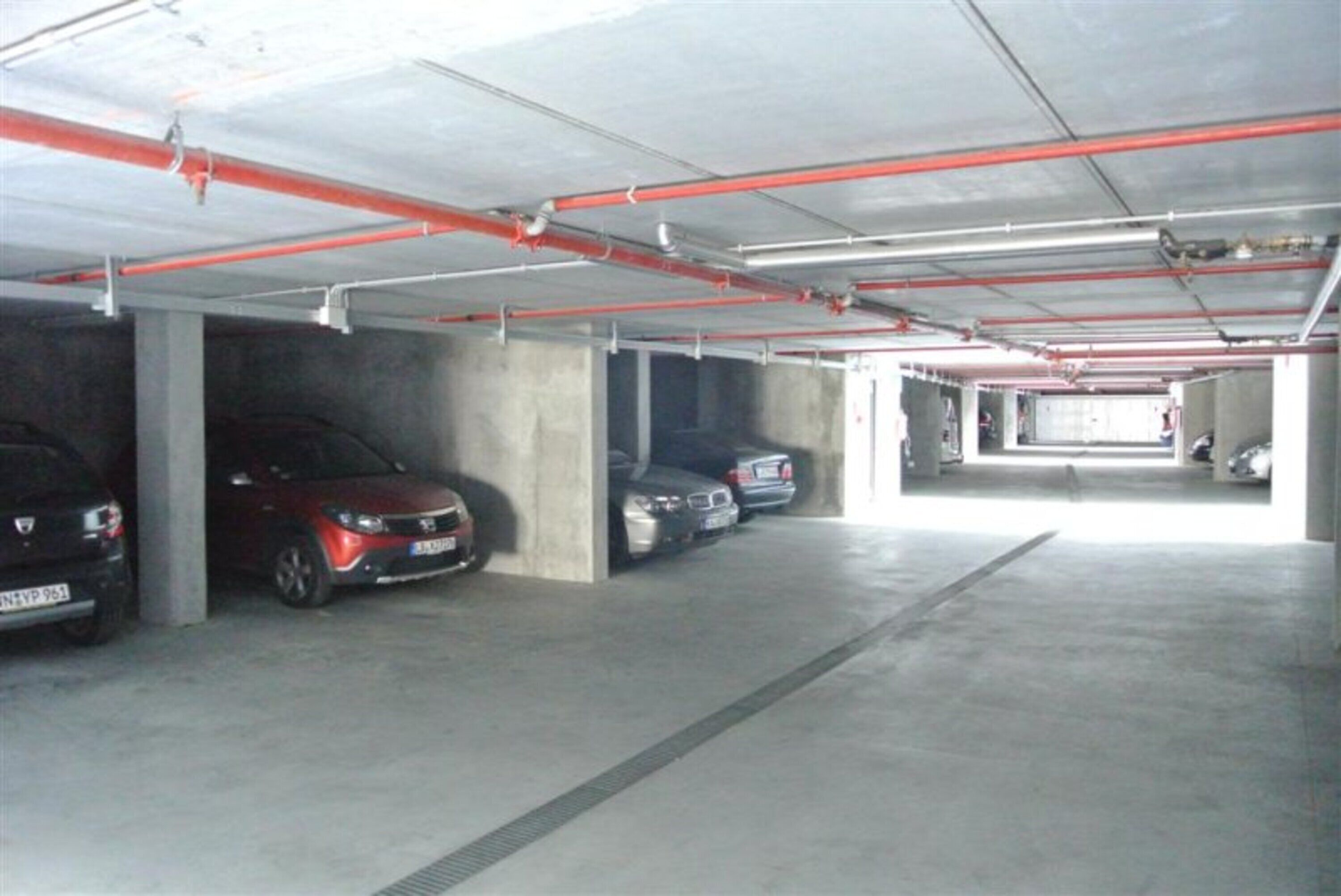A multi-level parking garage with concrete pillars and red pipes.