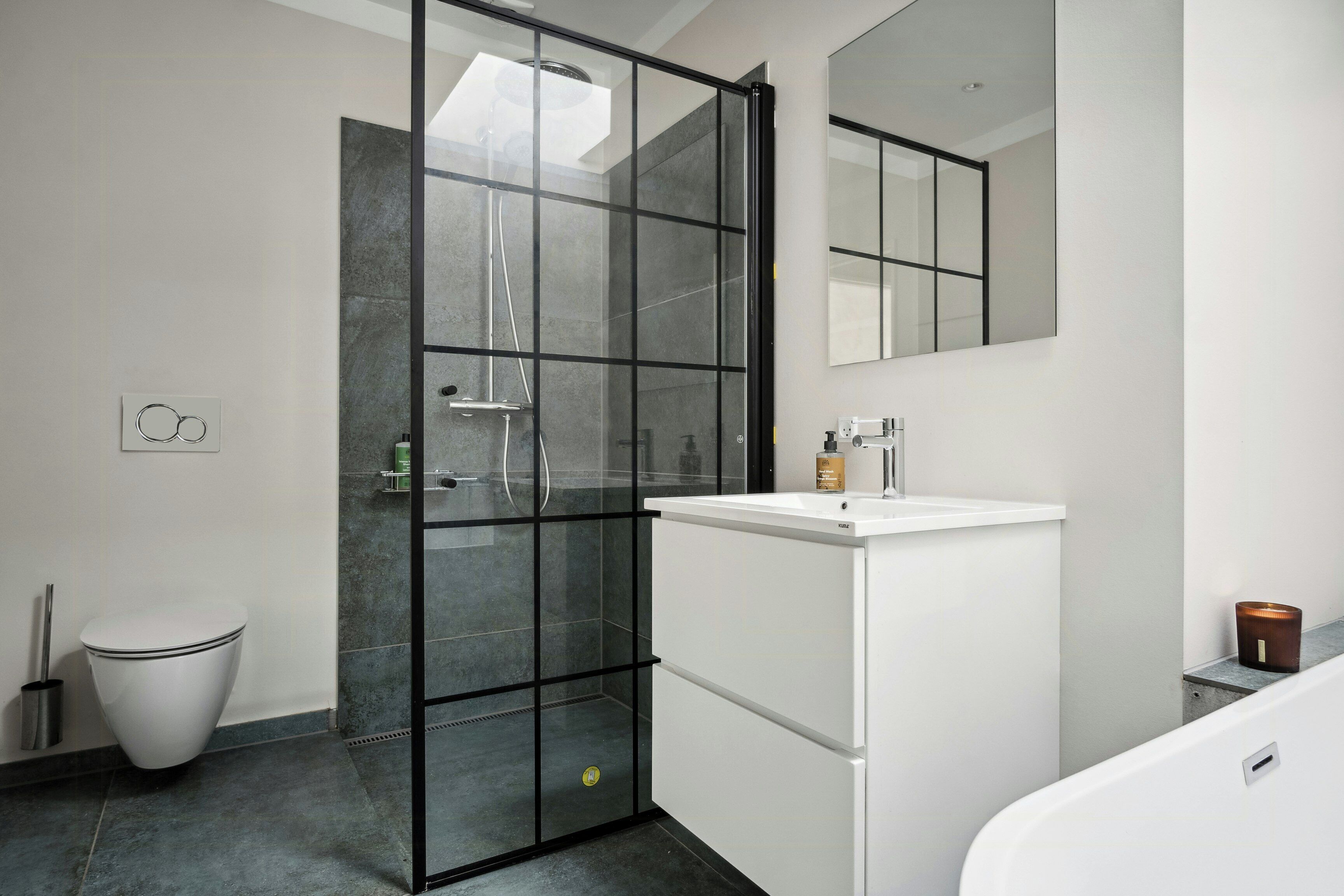 Un bagno moderno con box doccia in vetro, un lavandino bianco e uno specchio grande.
