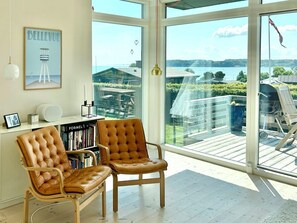 Ein Zimmer mit einem großen Fenster, einem Bücherregal, einem Ledersessel und einem gerahmten Bild an der Wand.