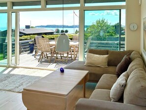 Ein geräumiges Wohnzimmer mit großem Fenster, einer Couch, einem Couchtisch und einem Essbereich mit Stühlen und Tisch.