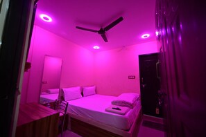 Ein Zimmer mit einem Bett, einem Schreibtisch, einem Stuhl, einem Deckenventilator und einer Tür.