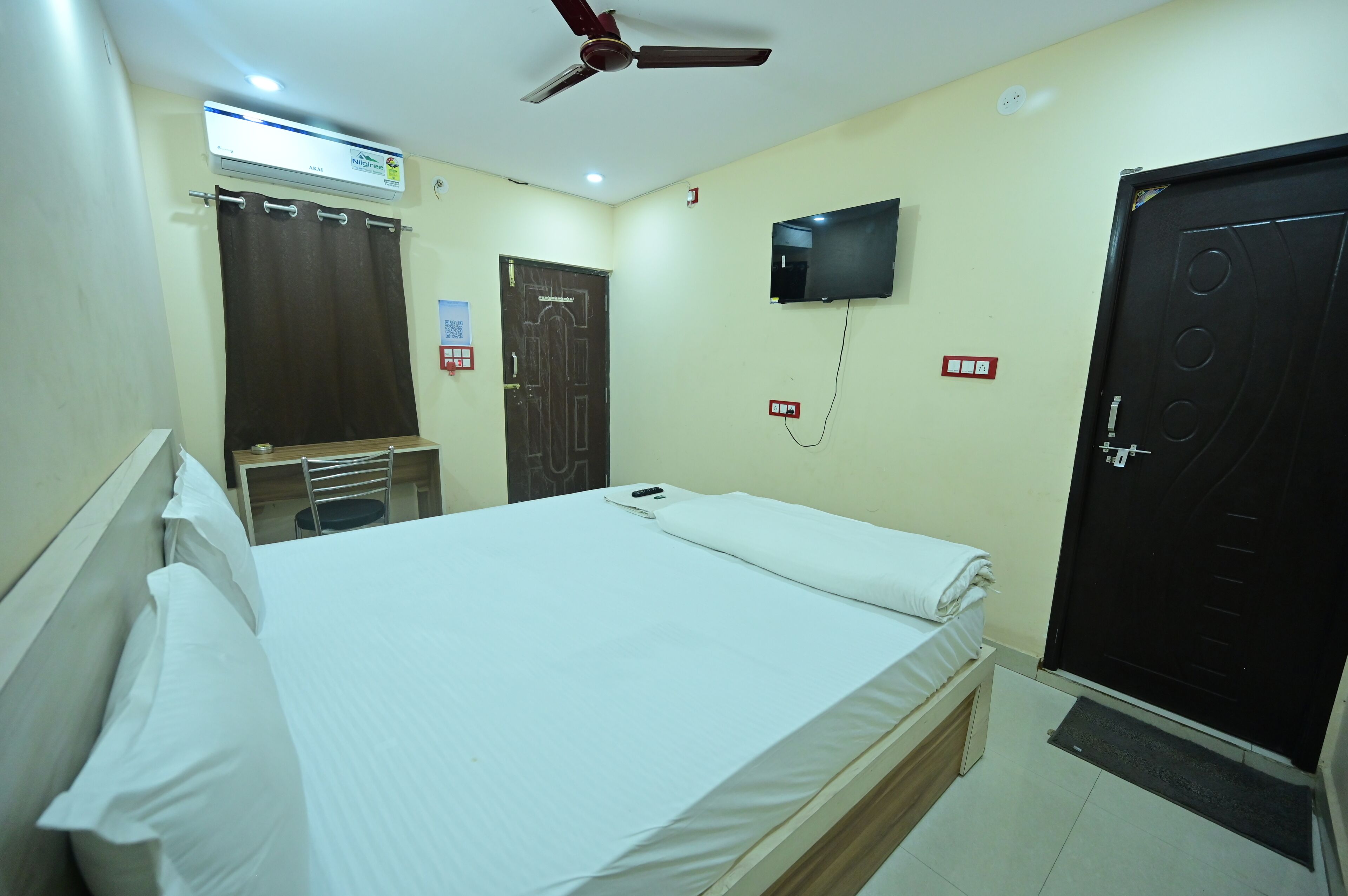 Una habitación de hotel con cama, ventilador de techo, televisión, puerta y ventana.