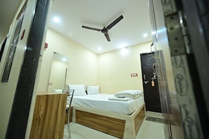 Une chambre Ă coucher comprenant un lit, un ventilateur de plafond, une commode en bois, un miroir et une porte avec une serrure.