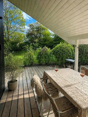 Eine Terrasse aus Holz mit Tisch, Stühlen, einem Blumentopf und einem Weinglas.