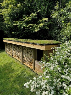 A garden with a wooden structure, a stone wall, and a variety of plants. - Modern family house near beach in Odsherred (Vig)