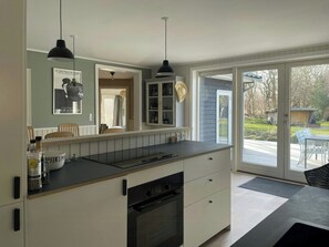A kitchen with a built-in oven, a countertop, and a dining area with a table and chairs. - Modern family house near beach in Odsherred (Vig)
