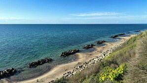 A coastal landscape with clear blue water, a sandy beach, and rocky outcrops. - Renovated wooden house at Vejby Beach (Vejby)