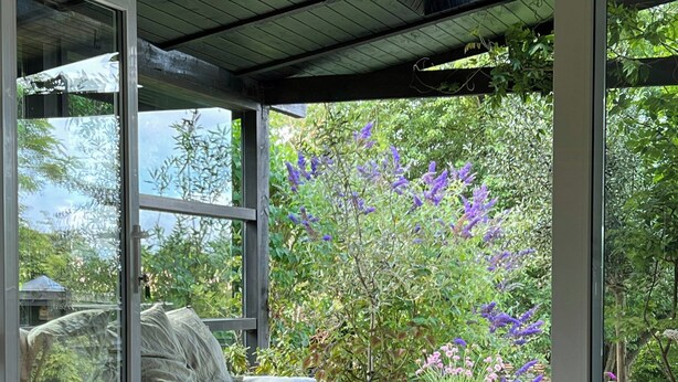 A room with a bed, a table, and a chair, with a view of a garden through large glass doors. - Renovated wooden house at Vejby Beach (Vejby)