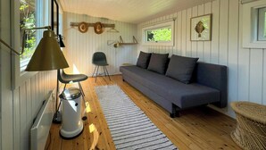 A room with a sofa, a chair, a lamp, a radiator, and a window. - Renovated wooden house at Vejby Beach (Vejby)