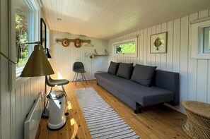 Ein Zimmer mit einer Schlafcouch, einem Sessel, einer Lampe, einer Heizung und einem Fenster.