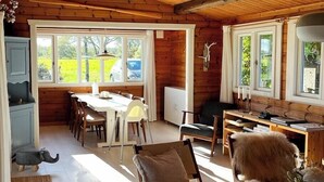 A wooden interior with a dining area, chairs, a table, and a view of the outdoors. - Log cabin with water views near Fjellerup beach (Ørsted)
