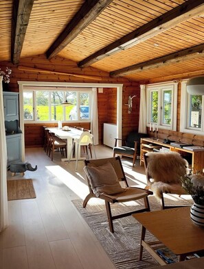 Ein Holzinnenraum mit Essbereich, Stühlen, einem Tisch und Blick ins Freie.
