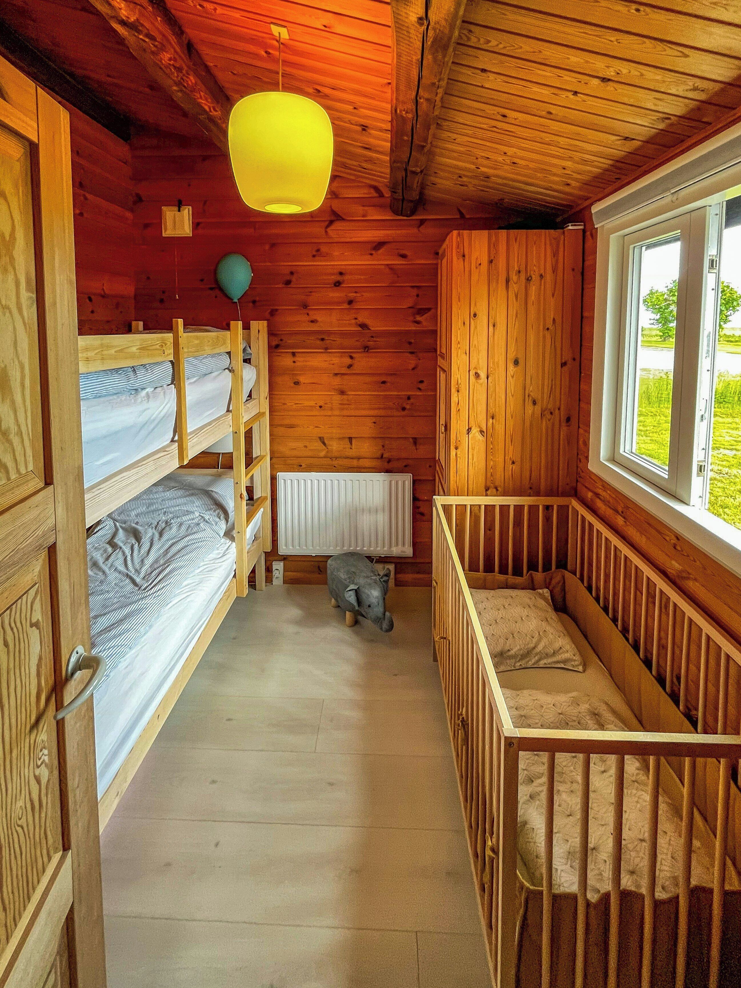 A cabin with a wooden interior, bunk beds, a radiator, and a window with a view of greenery.
