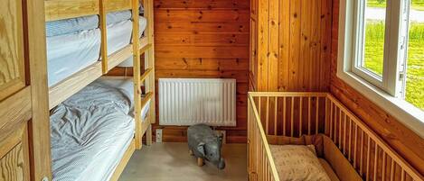 A cabin with a wooden interior, bunk beds, a radiator, and a window with a view of greenery.