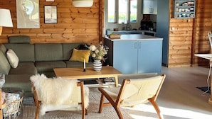 A cozy cabin interior with a wooden interior, a dining area with a table and chairs, a sofa, and a kitchen area with cabinets and a sink. - Log cabin with water views near Fjellerup beach (Ørsted)
