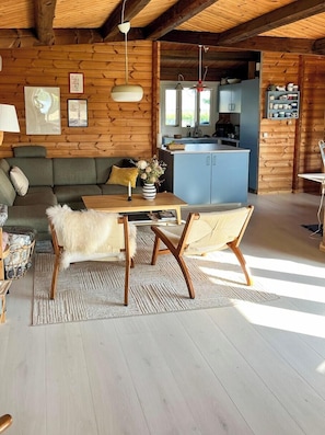 Ein gemütliches Blockhaus-Interieur mit Holzausbau, einem Essbereich mit Tisch und Stühlen, einer Couch sowie einer Küchenzeile mit Schränken und Spüle.
