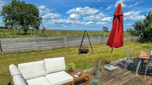 A wooden deck with a white sofa, a swing, and a red umbrella. - Log cabin with water views near Fjellerup beach (Ørsted)