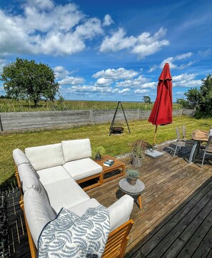 Eine Holzterrasse mit einer weißen Couch, einer Schaukel und einem roten Sonnenschirm.