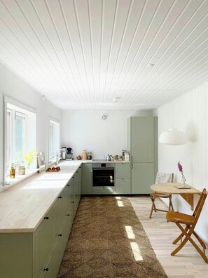 Eine moderne Küche mit hellem Holzdeckenbau, einer zentralen Kochinsel und einem Essbereich mit Tisch und Stühlen.