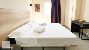 A hotel room with a bed, a desk, a chair, a window, and a curtain. - HOTEL LA MARINA (Elche)