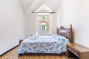 Een slaapkamer met een bed, een houten dressoir en een raam met uitzicht op groen.
