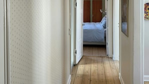 A hallway with wooden flooring, white walls with a dotted pattern, and a door leading to a bedroom with a bed and a wardrobe. - Design flat between Frederiksberg and Vesterbro (København)