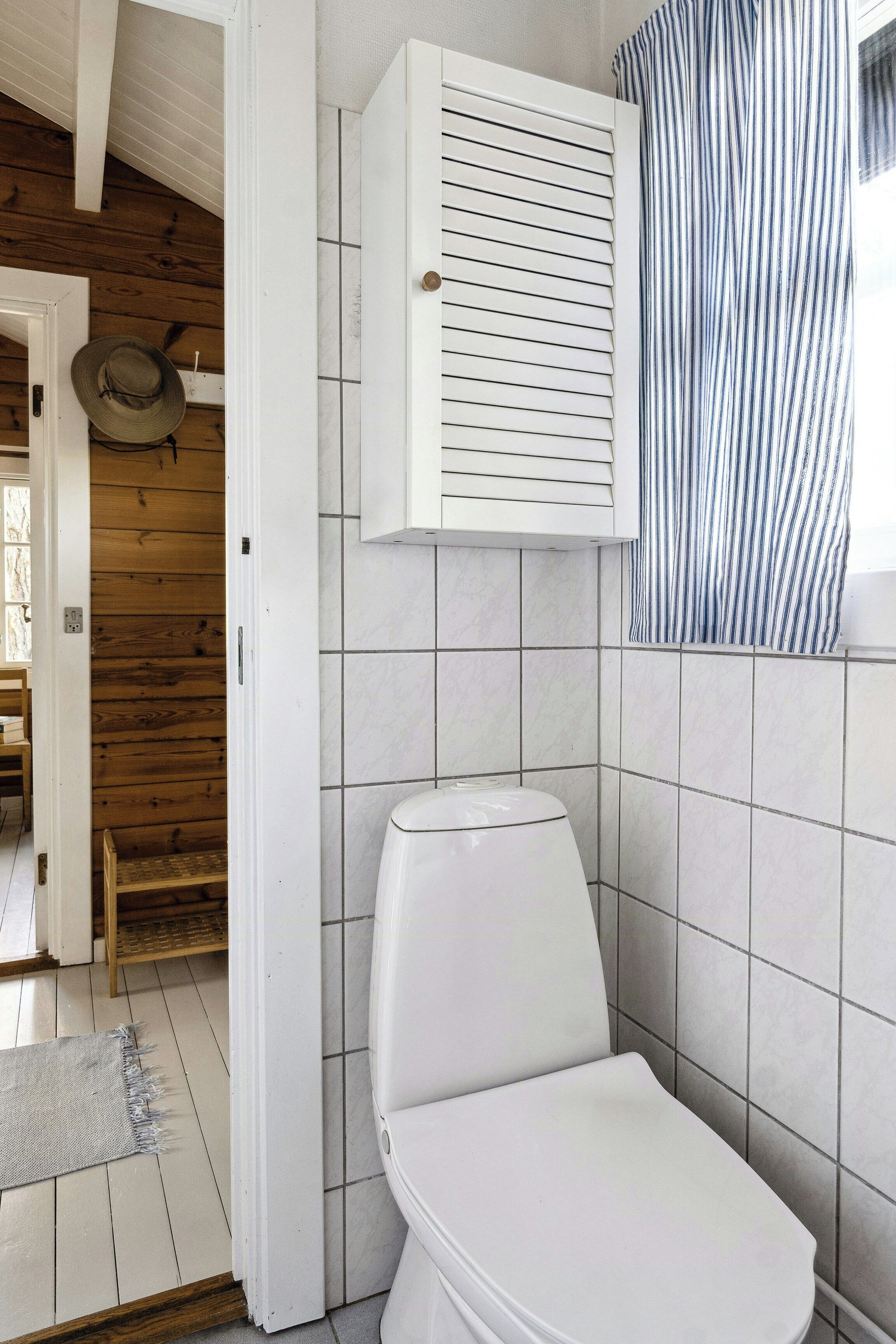 Un bagno con un WC bianco, una porta in legno e un muro rivestito di piastrelle.