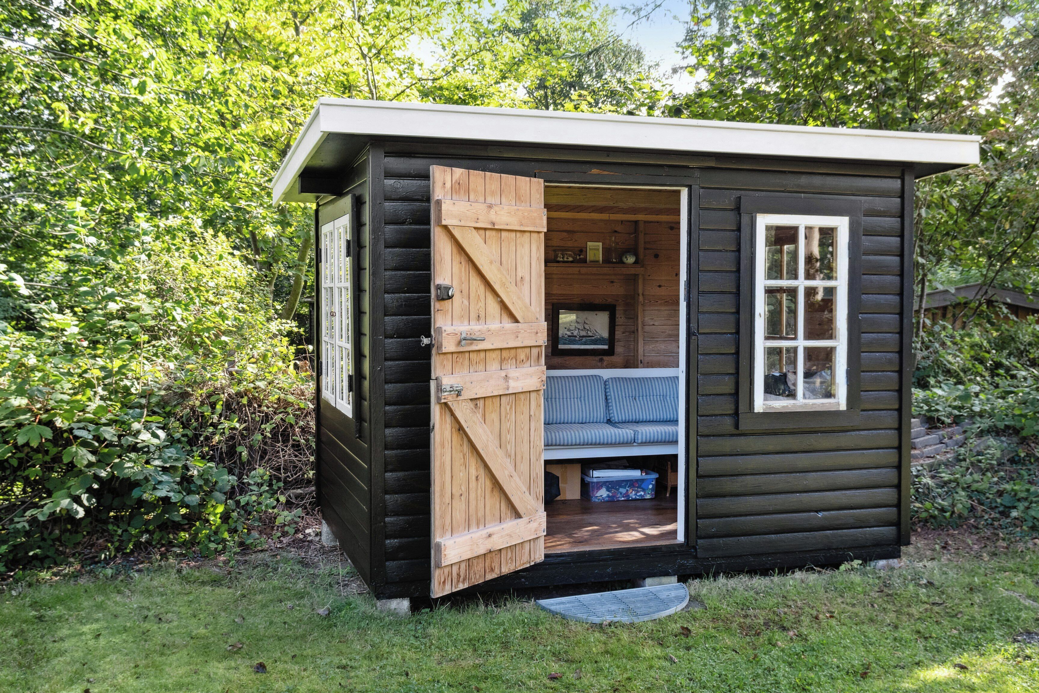 A small wooden cabin with a sliding door, a window, and a bench inside.