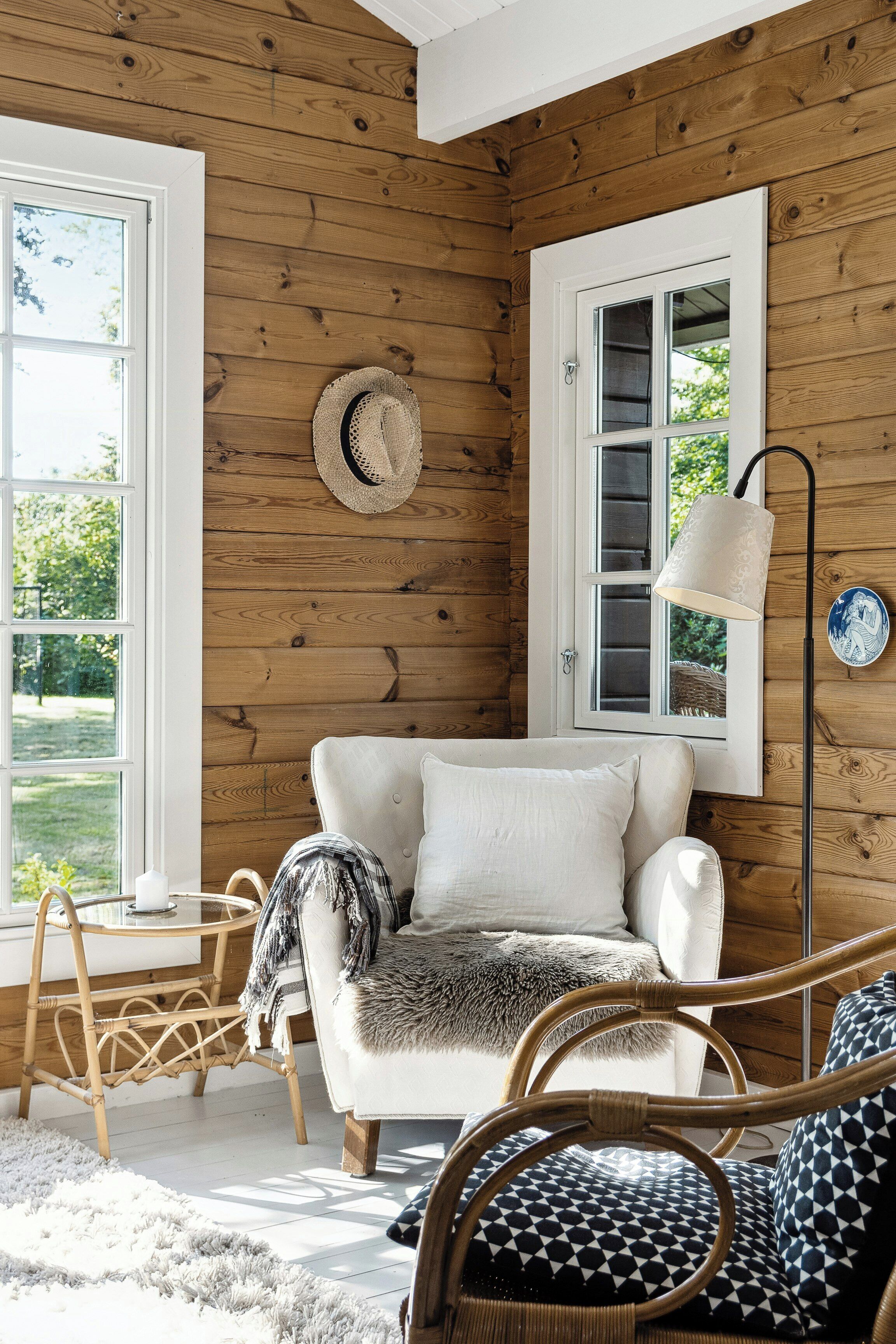 A cozy room with a wooden wall, a white sofa, a rattan chair, and a floor lamp.