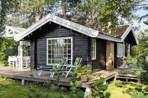Eine Hütte mit Veranda, grünen Stühlen und einem kleinen Tisch.