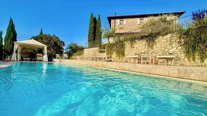 A clear swimming pool with lounge chairs and a covered area, surrounded by stone walls and vegetation. - Villa with infinity pool in the Tuscan hills (Rignano sull'arno)