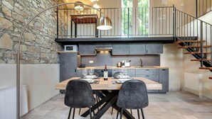 A modern kitchen with a stone wall, a dining table with chairs, and a staircase. - Villa with infinity pool in the Tuscan hills (Rignano sull'arno)