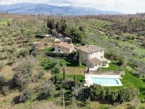 Una villa in pietra con piscina, immersa in un paesaggio rigoglioso e con montagne sullo sfondo.