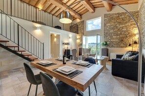 Un'ampia zona giorno con un tavolo da pranzo in legno, sedie nere, una scala e una parete in pietra.