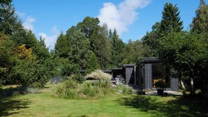 Un bâtiment moderne de style cabane, doté d’un espace extérieur couvert et entouré d’une forêt dense.