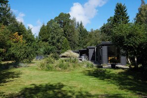 Ein modernes Blockhaus mit überdachter Terrasse, umgeben von dichtem Wald.