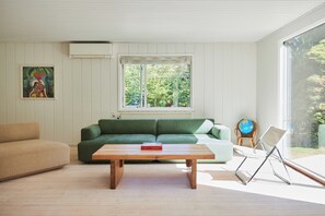 Ein Wohnzimmer mit einem grünen Sofa, einem hölzernen Couchtisch, einem beigen Sofa, einem Globus und einem Fenster mit Blick auf Bäume.