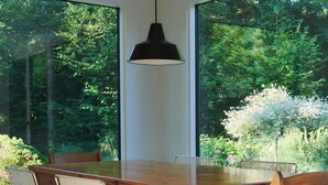 Une table à manger en bois, des chaises en métal, de grandes fenêtres et un luminaire suspendu.