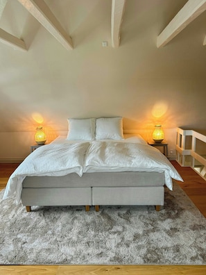 Un dormitorio con una cama grande, dos lámparas de noche, piso de madera y barandilla blanca.
