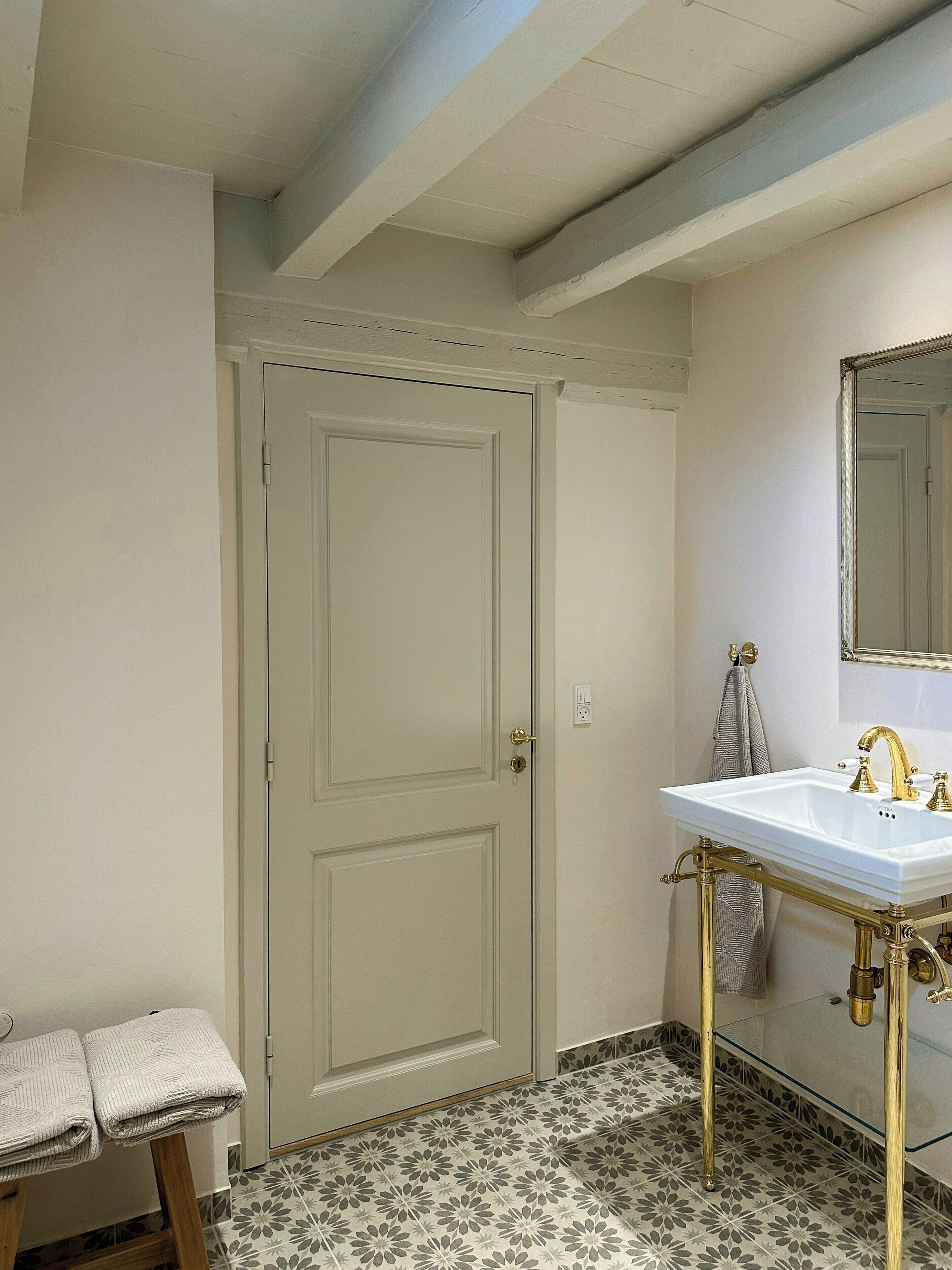Une salle de bain avec une porte blanche, un lavabo doté de robinetterie dorée et un carrelage au sol à motifs.