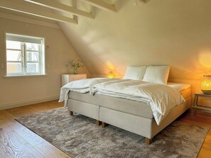 Une chambre à coucher avec un lit, une table de chevet, une lampe, une fenêtre et une petite table.
