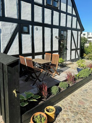 Un bâtiment à colombages doté d’un patio comprenant une table et des chaises en bois, des plantes en pot et un chemin en pierre.