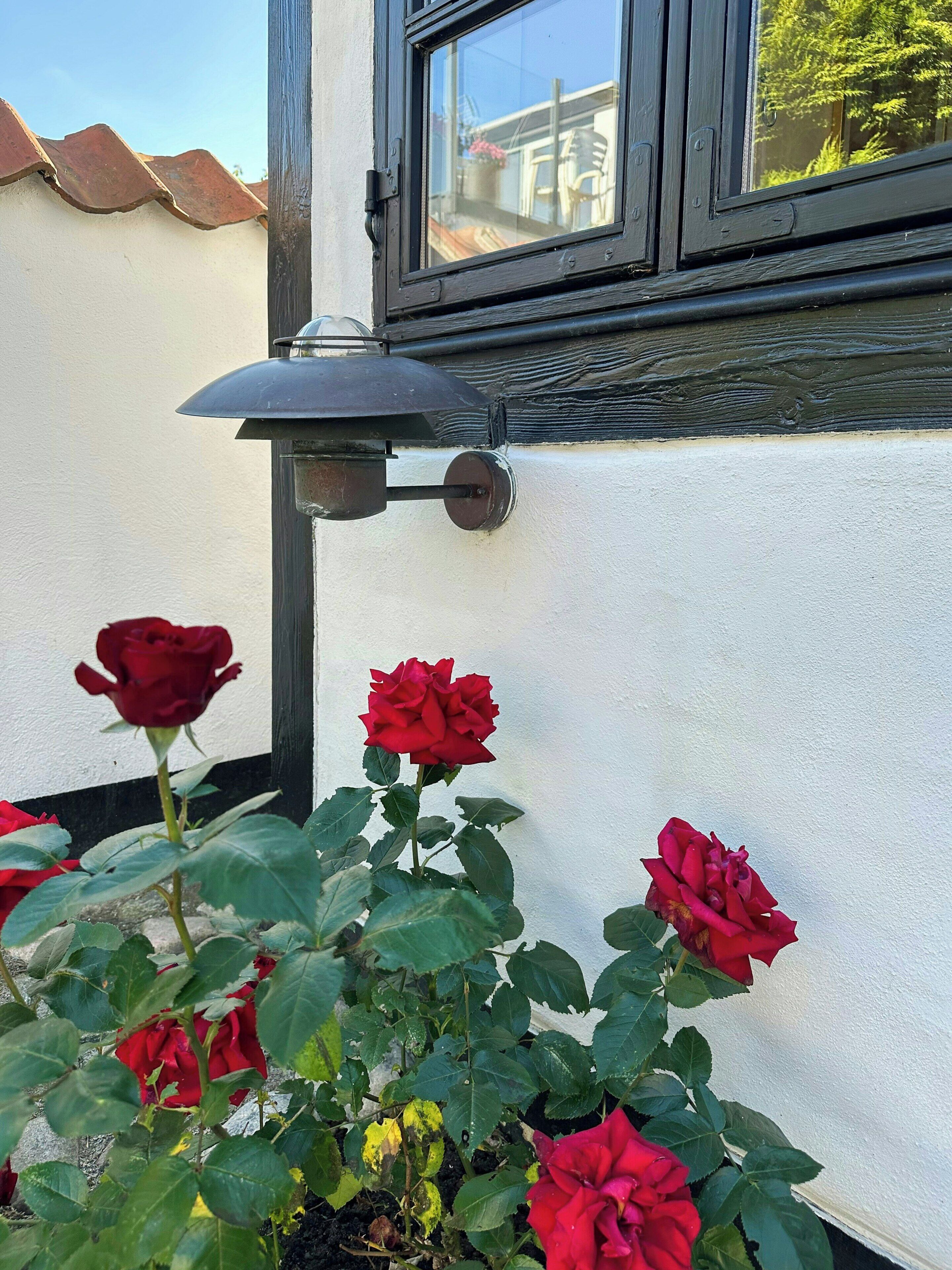 Un edificio blanco con una ventana, una lámpara de pared y rosas rojas.